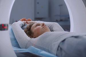 Woman lies on CT or PET or MRI scan bed and moves in machine